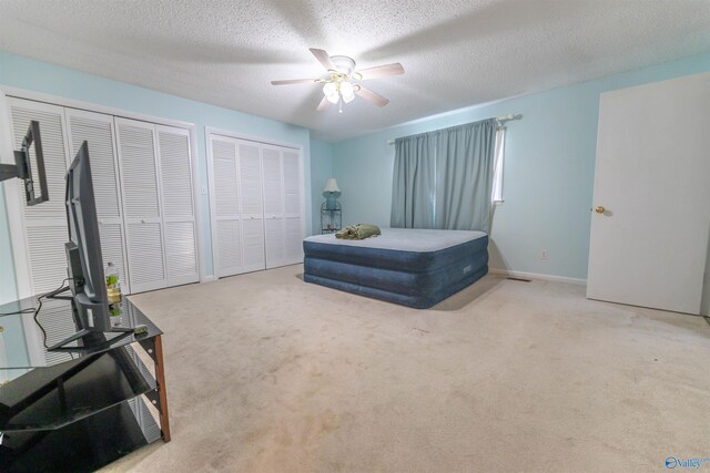 carpeted bedroom with ceiling fan, two closets, and a textured ceiling