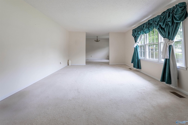 carpeted empty room featuring an inviting chandelier, baseboards, a textured ceiling, and visible vents