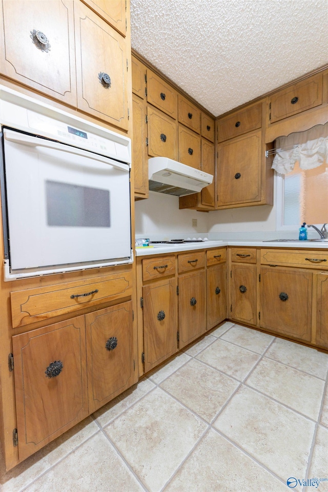 kitchen with brown cabinets, white appliances, light countertops, a textured ceiling, and under cabinet range hood