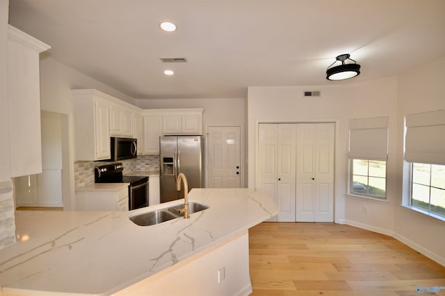 kitchen featuring white cabinetry, sink, light stone countertops, appliances with stainless steel finishes, and light wood-type flooring