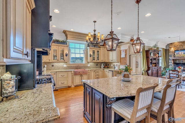 kitchen with a kitchen island, light stone countertops, ornamental molding, and light wood-type flooring