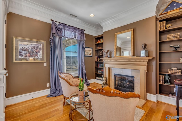 sitting room with a tile fireplace, ornamental molding, and light hardwood / wood-style flooring