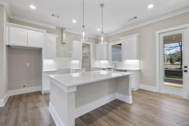 kitchen with white cabinets, decorative light fixtures, a kitchen island, and light hardwood / wood-style flooring