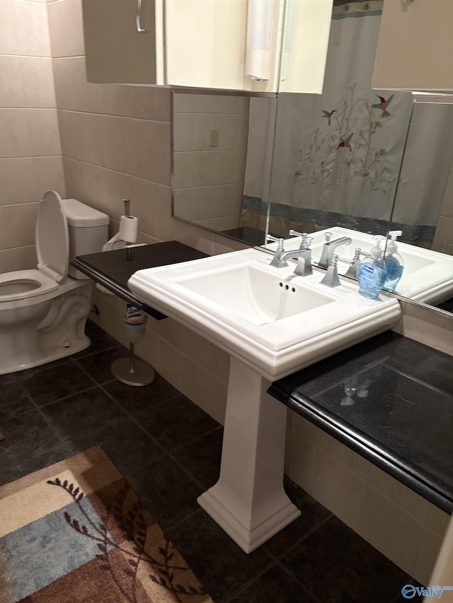 bathroom featuring toilet, a sink, tile patterned flooring, and tile walls