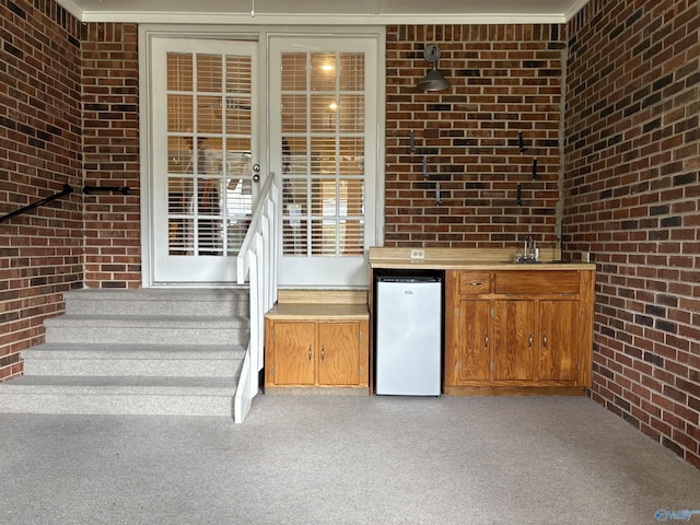 interior space featuring refrigerator, indoor bar, light carpet, and brick wall
