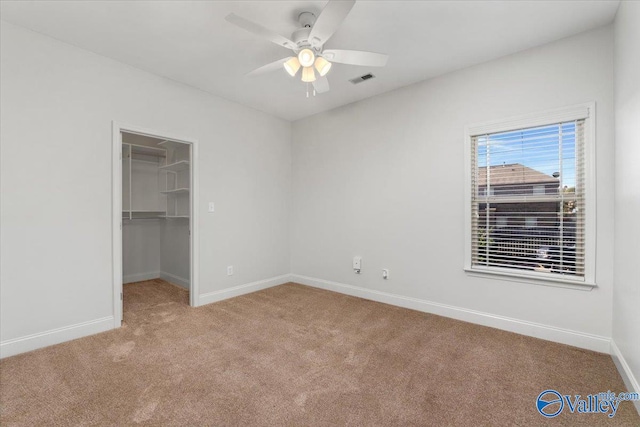 unfurnished bedroom with light carpet, a walk in closet, a closet, and ceiling fan