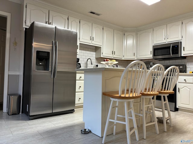 kitchen featuring a breakfast bar area, white cabinets, tasteful backsplash, and stainless steel appliances