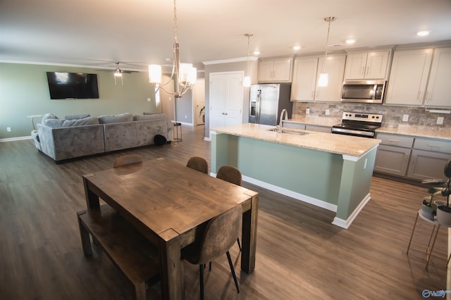 kitchen with an island with sink, stainless steel appliances, light stone countertops, sink, and pendant lighting