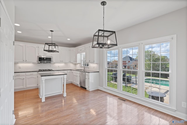 kitchen featuring white cabinets, sink, appliances with stainless steel finishes, decorative light fixtures, and a kitchen island