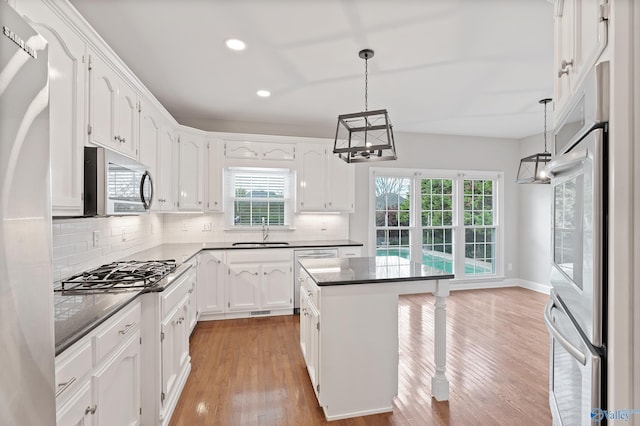 kitchen with sink, a center island, stainless steel appliances, decorative light fixtures, and light wood-type flooring