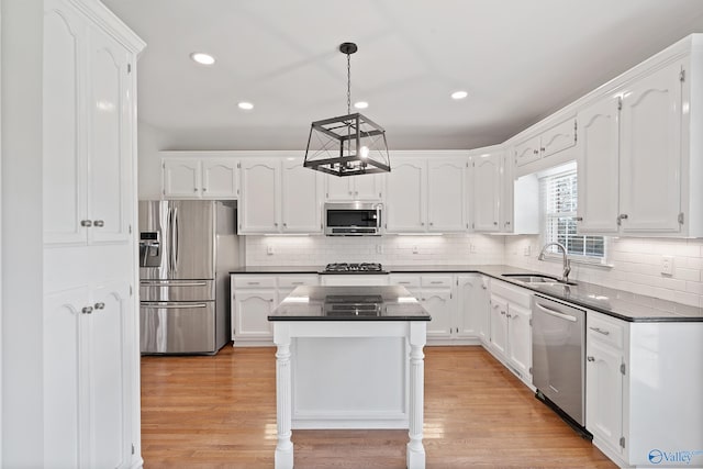 kitchen featuring appliances with stainless steel finishes, light wood-type flooring, sink, white cabinets, and a center island