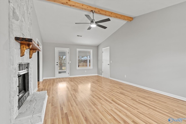 unfurnished living room featuring ceiling fan, a large fireplace, light wood-type flooring, and beam ceiling