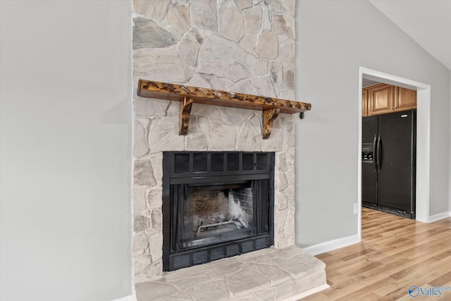 details with black refrigerator with ice dispenser, a fireplace, and hardwood / wood-style flooring