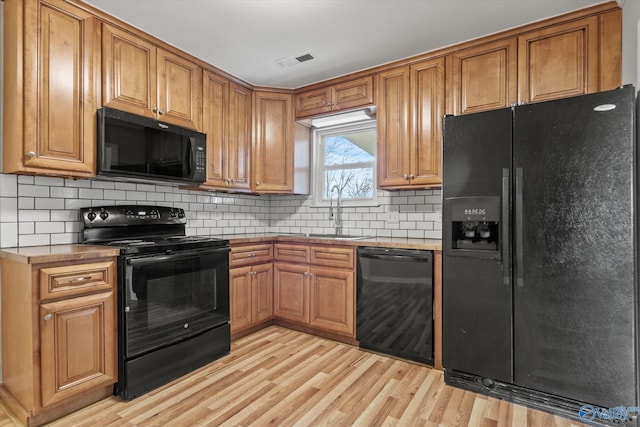 kitchen with tasteful backsplash, sink, black appliances, and light wood-type flooring