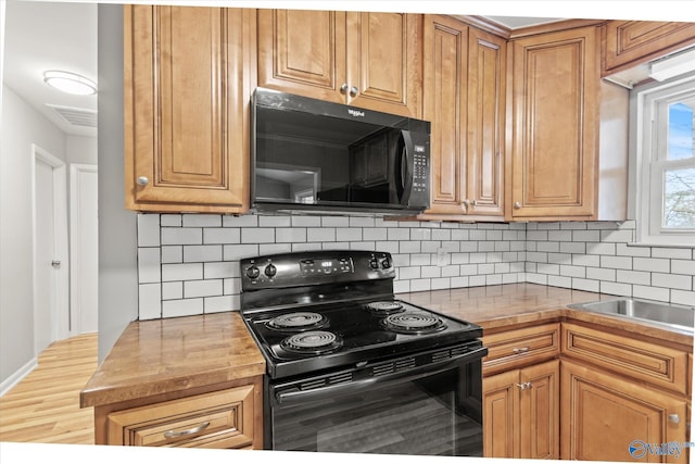 kitchen featuring black appliances, decorative backsplash, butcher block countertops, and hardwood / wood-style floors