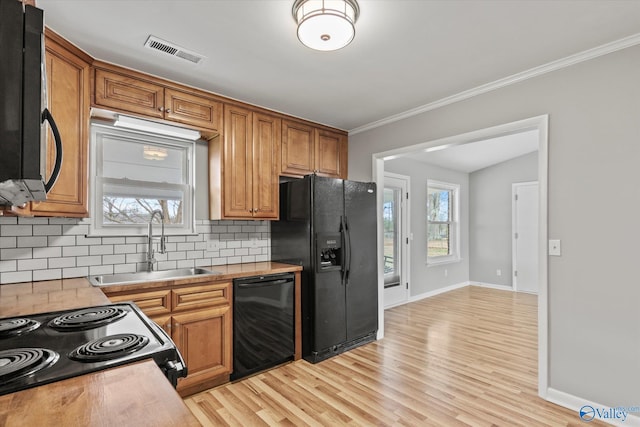 kitchen with black appliances, backsplash, sink, and light hardwood / wood-style flooring