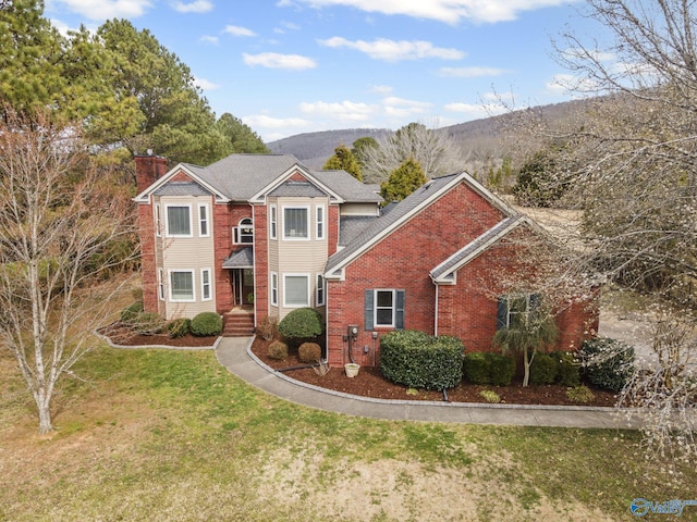 view of front of home with a front yard, a mountain view, brick siding, and a chimney