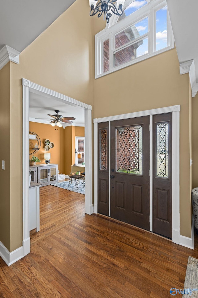 entryway with ceiling fan with notable chandelier, a high ceiling, wood finished floors, and baseboards