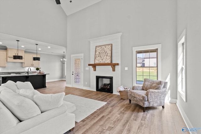 living room featuring light wood-type flooring, a large fireplace, a notable chandelier, sink, and high vaulted ceiling