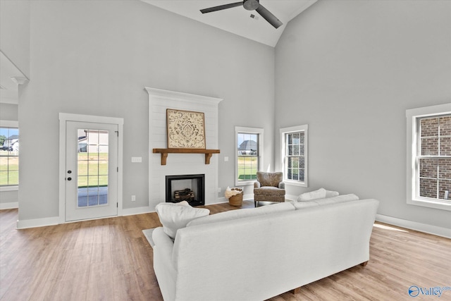 living room with a large fireplace, ceiling fan, high vaulted ceiling, and light hardwood / wood-style floors