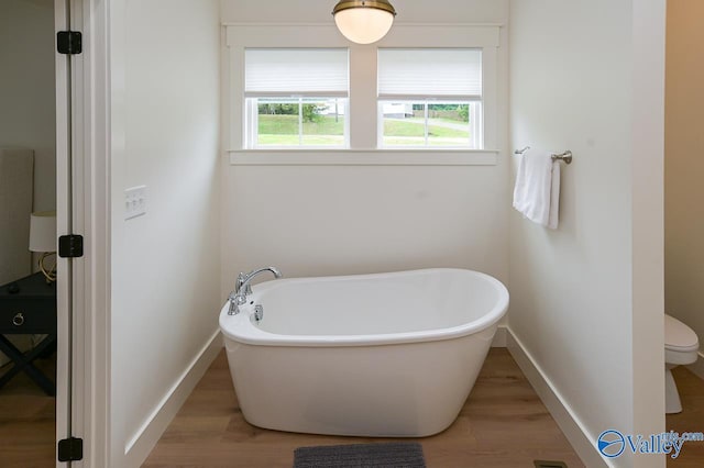 bathroom featuring a soaking tub, baseboards, wood finished floors, and toilet