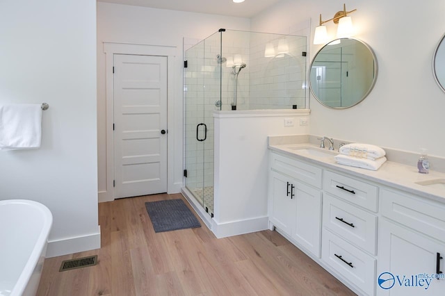 bathroom with a shower stall, wood finished floors, a sink, double vanity, and visible vents