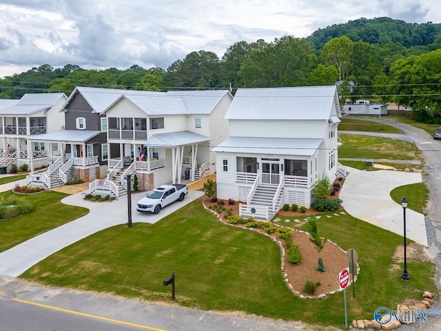 view of front of home with concrete driveway, a front lawn, stairs, and metal roof