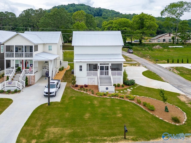 back of property with a porch, metal roof, concrete driveway, a lawn, and stairs
