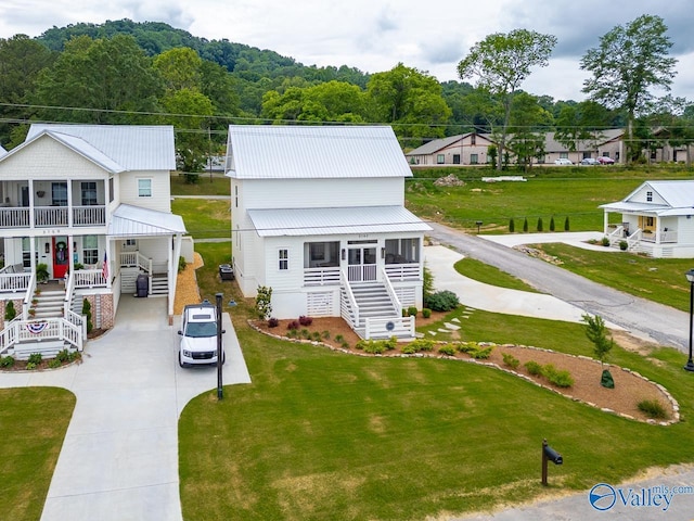 exterior space with stairway, concrete driveway, covered porch, a front yard, and metal roof