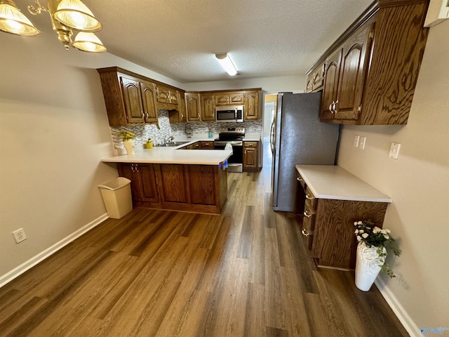 kitchen with a peninsula, a sink, stainless steel appliances, light countertops, and backsplash