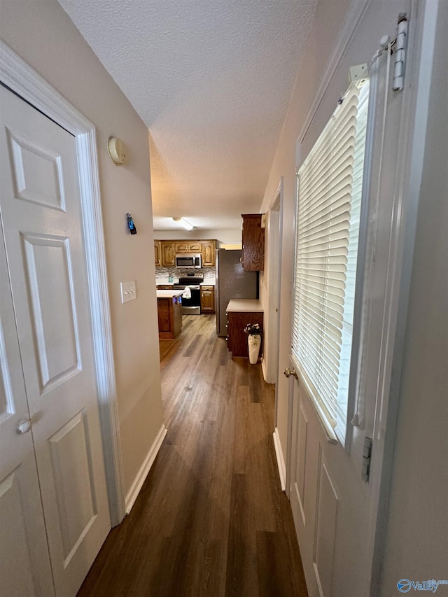 hallway with dark wood-style flooring, a textured ceiling, and baseboards