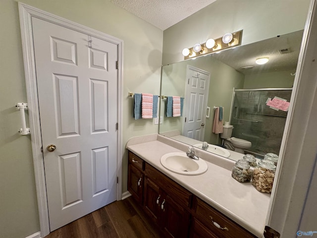 bathroom with a textured ceiling, toilet, wood finished floors, vanity, and a shower stall