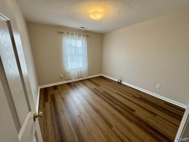 spare room featuring dark wood-style floors, visible vents, baseboards, and a textured ceiling