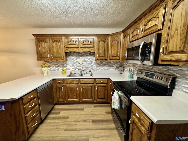 kitchen featuring light countertops, appliances with stainless steel finishes, a sink, light wood-type flooring, and a peninsula