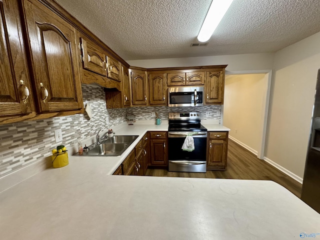 kitchen with a sink, light countertops, appliances with stainless steel finishes, dark wood-style floors, and tasteful backsplash