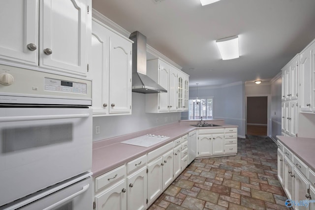 kitchen featuring a peninsula, white appliances, white cabinets, light countertops, and wall chimney exhaust hood