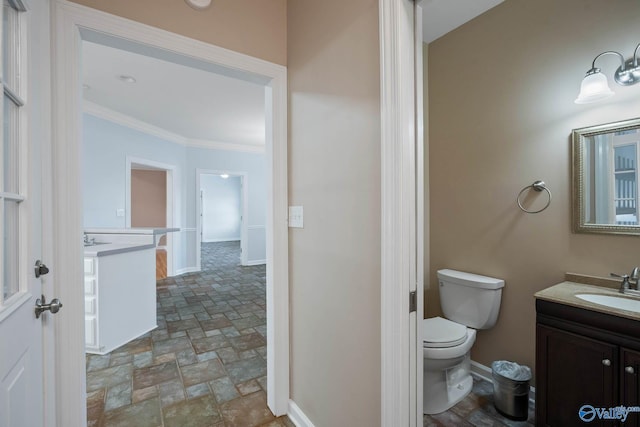 bathroom featuring toilet, vanity, baseboards, stone finish flooring, and crown molding