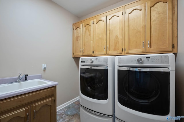 laundry room with cabinet space, baseboards, washer and clothes dryer, stone tile flooring, and a sink