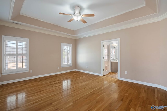 unfurnished room featuring light wood-style floors, a raised ceiling, ornamental molding, and baseboards