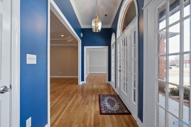 entryway with baseboards, crown molding, light wood finished floors, and an inviting chandelier