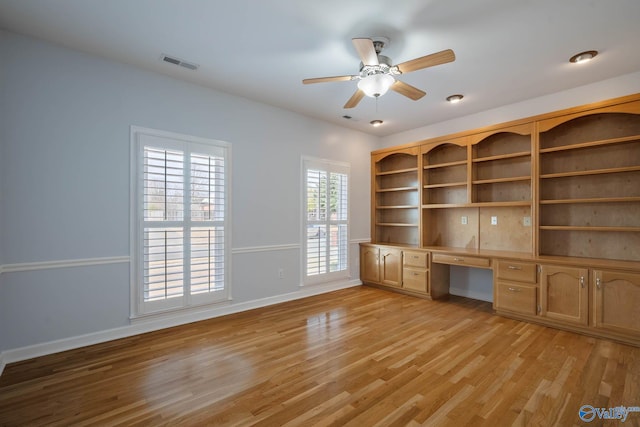 unfurnished office featuring visible vents, baseboards, ceiling fan, light wood-style floors, and built in desk