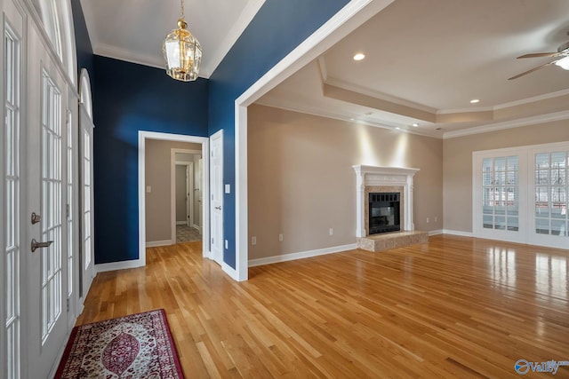 unfurnished living room with crown molding, a fireplace, light wood finished floors, a raised ceiling, and baseboards