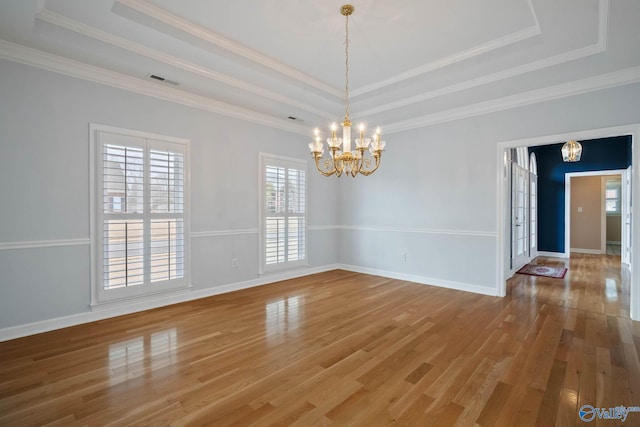 empty room featuring light wood-style flooring, visible vents, a tray ceiling, and a chandelier