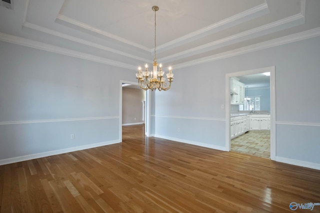 unfurnished room with a chandelier, baseboards, light wood-style floors, a tray ceiling, and crown molding