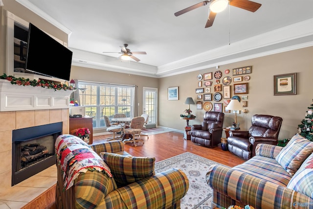 living room featuring ceiling fan, light hardwood / wood-style flooring, a tile fireplace, and a tray ceiling