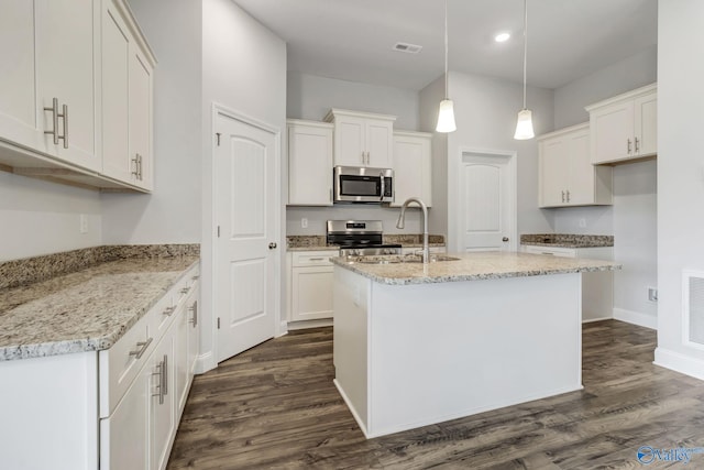 kitchen with appliances with stainless steel finishes, a kitchen island with sink, hanging light fixtures, light stone countertops, and white cabinets