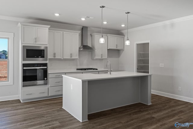 kitchen featuring wall chimney range hood, an island with sink, crown molding, built in microwave, and stainless steel oven