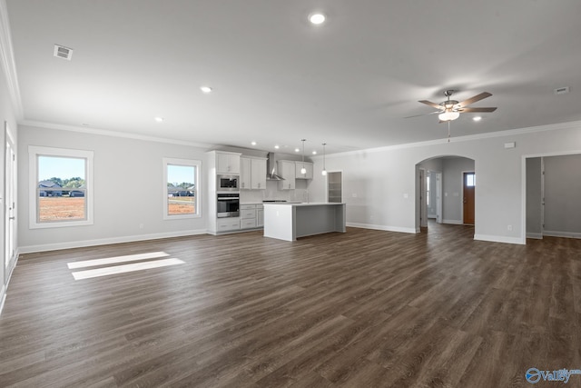 unfurnished living room featuring arched walkways, ceiling fan, baseboards, and dark wood-style flooring