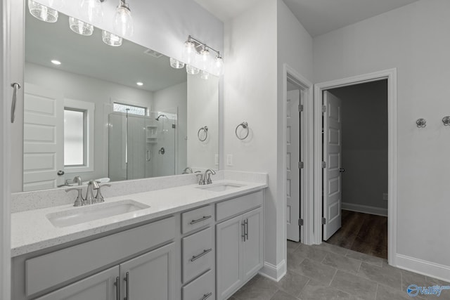 bathroom featuring a shower stall, double vanity, baseboards, and a sink