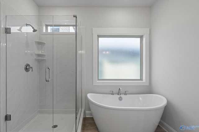 full bathroom with a shower stall, a freestanding bath, and baseboards